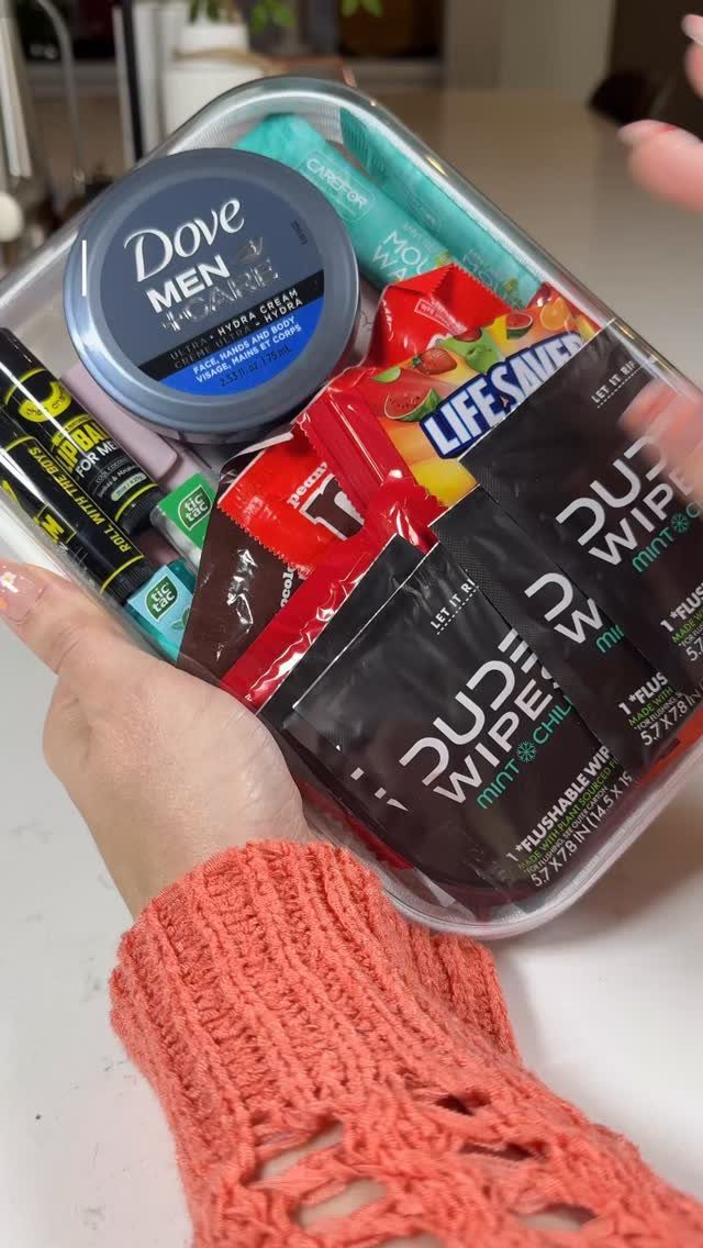 Clear plastic bin filled with men's grooming products and snacks held by hands.