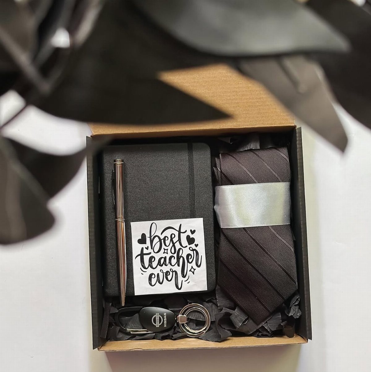 Gift box for a teacher containing a notebook, pen, striped tie, and keychain.
