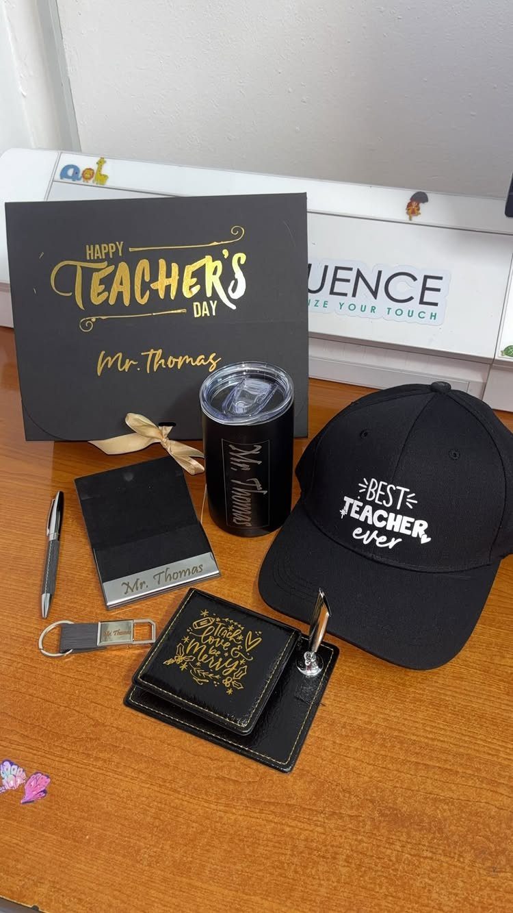 Teacher gift set with black cap, tumbler, wallet, and card on wooden table
