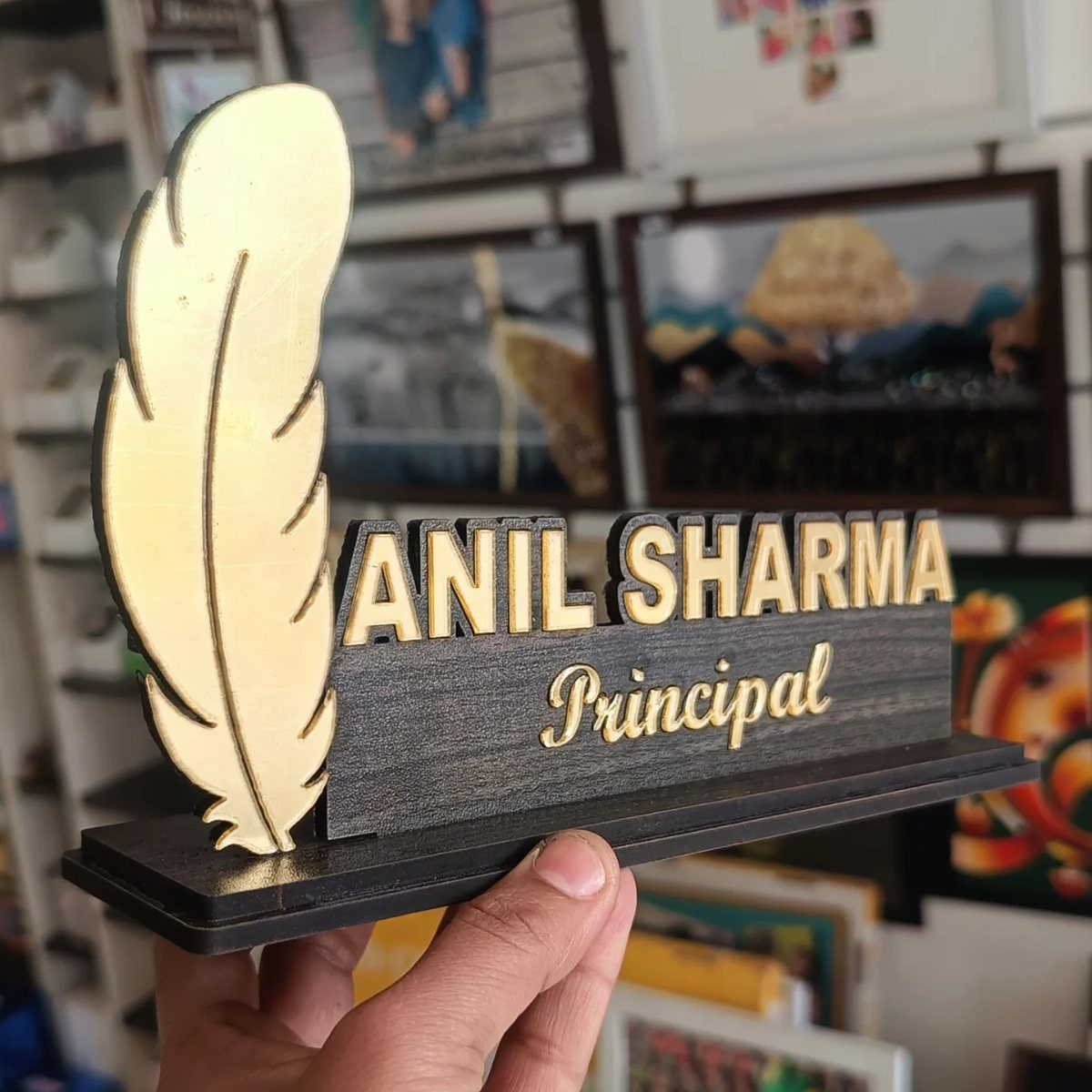 Desk name plate with gold feather and text Anil Sharma Principal on wood