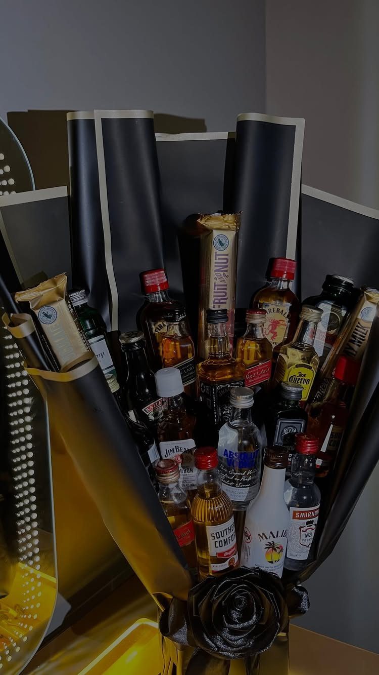Liquor bottle bouquet wrapped in black and gold paper with a black rose.