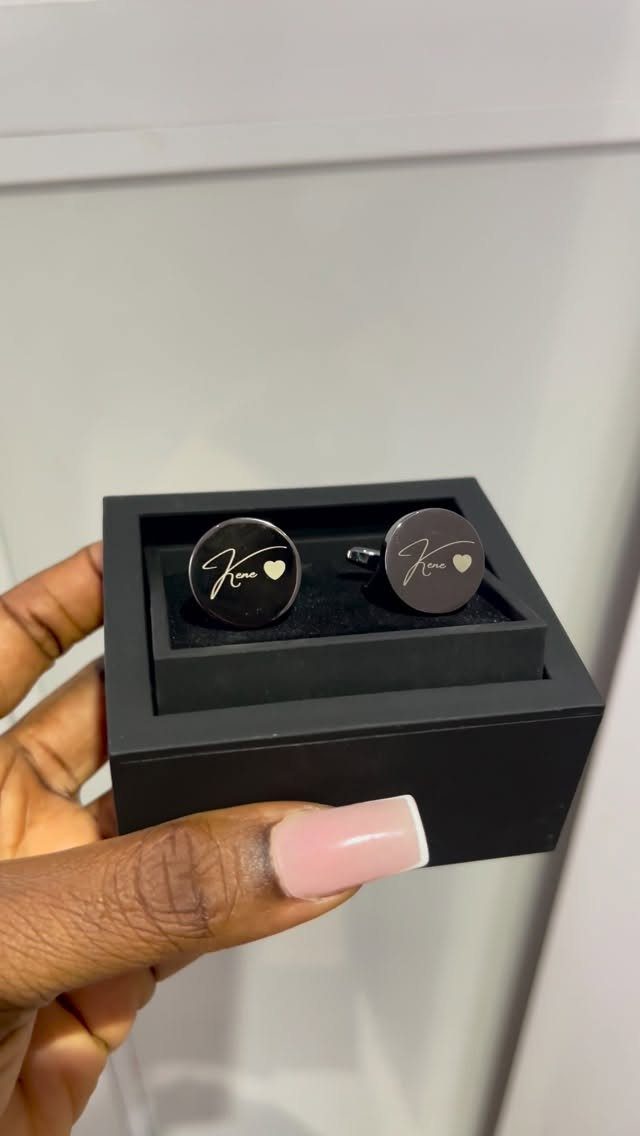 Two round black personalized cufflinks with gold initials in a black gift box.