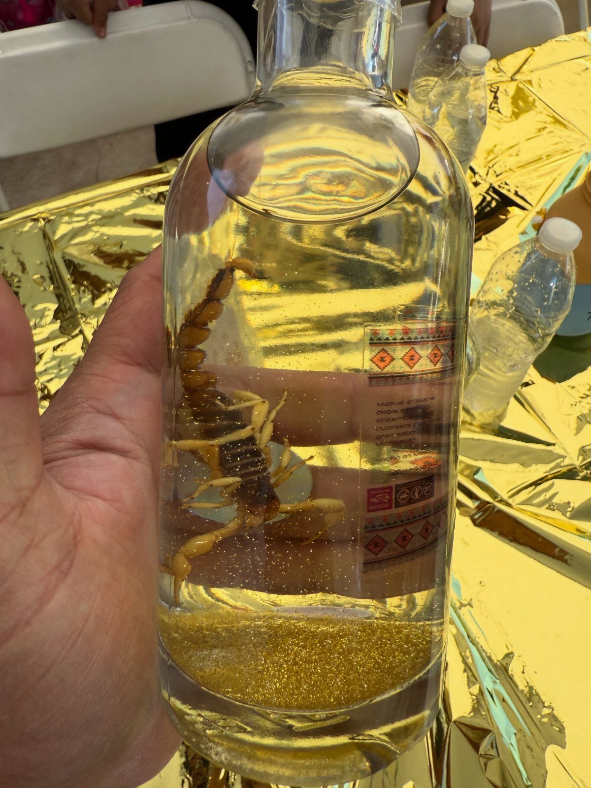 Glass bottle with a scorpion inside filled with yellow liquid on gold background