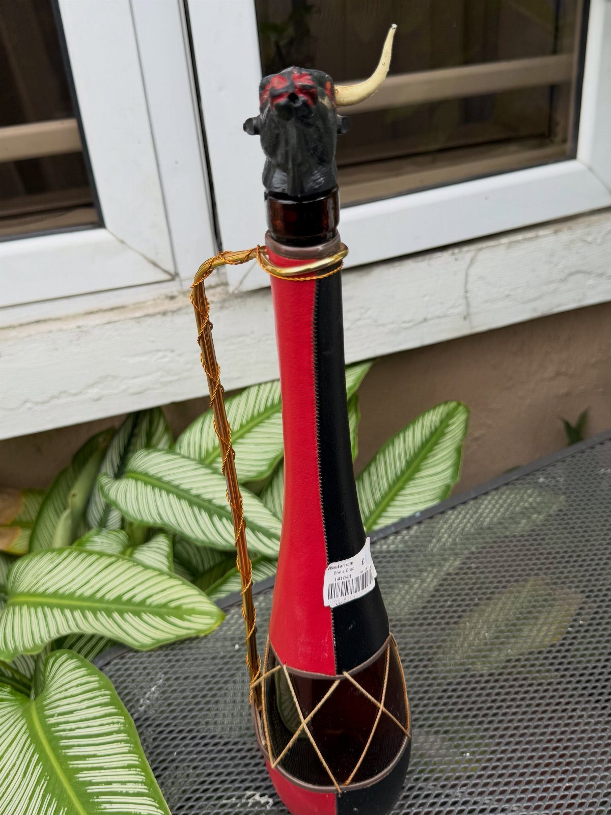 Red and black striped bottle with a bull figurine stopper and gold cord.