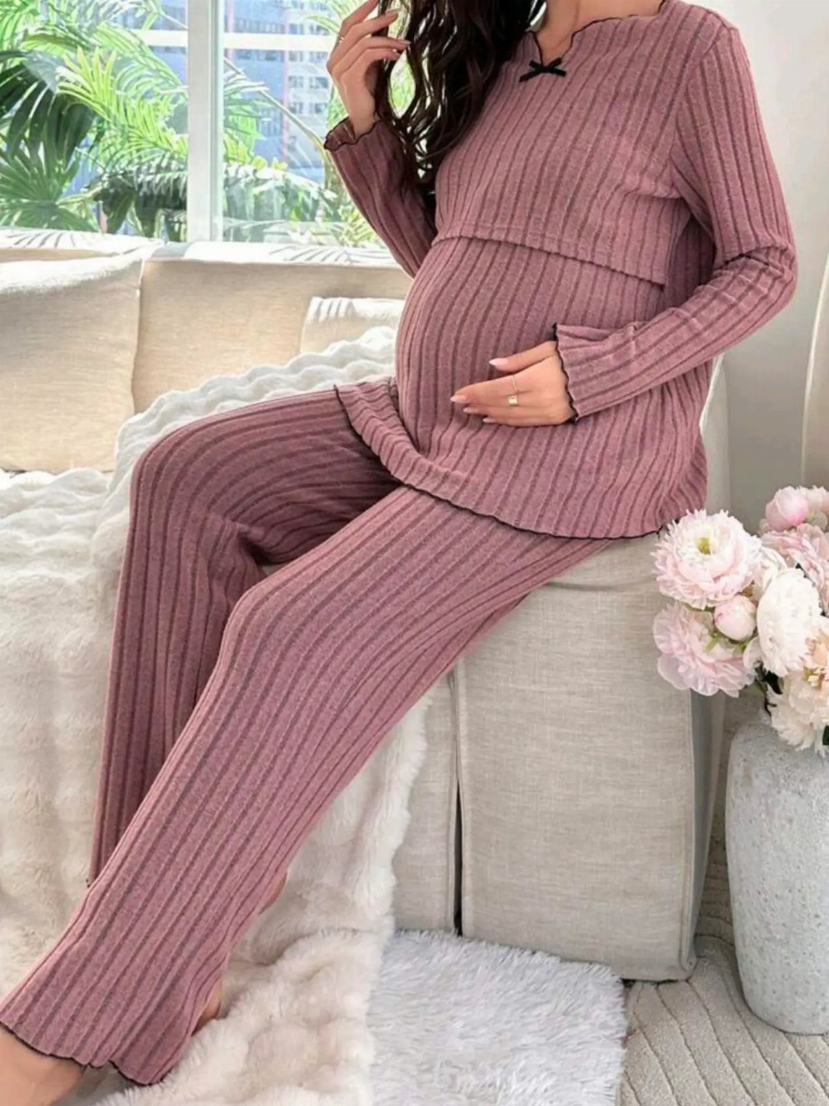 Pregnant woman wearing a mauve ribbed knit loungewear set sitting on a white sofa.
