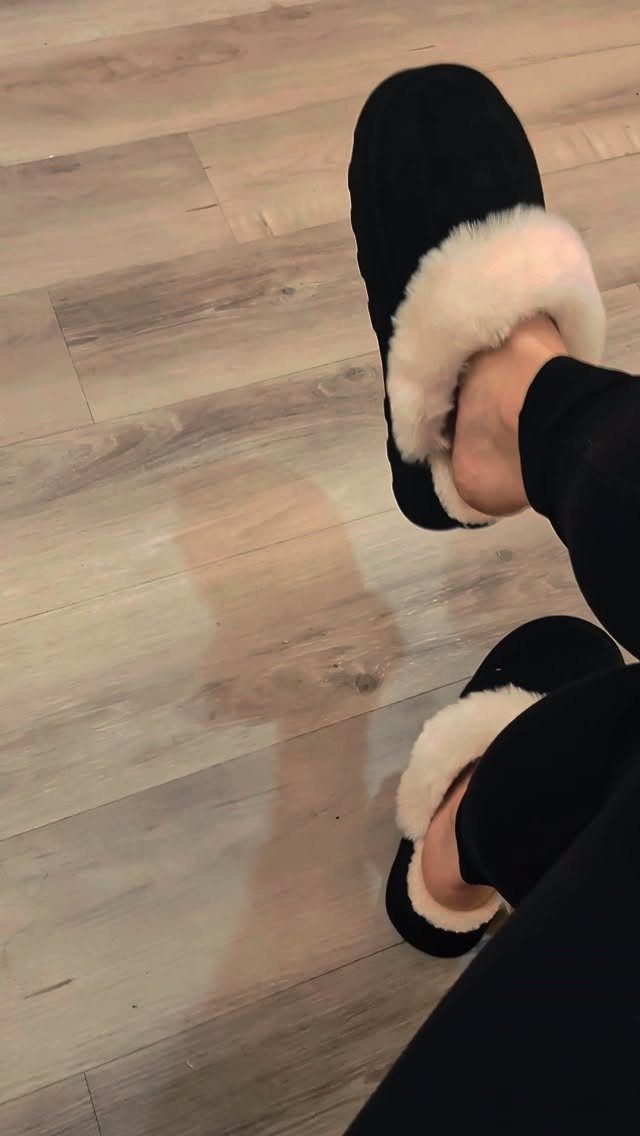 Black slippers with white faux-fur lining on a light wood floor.