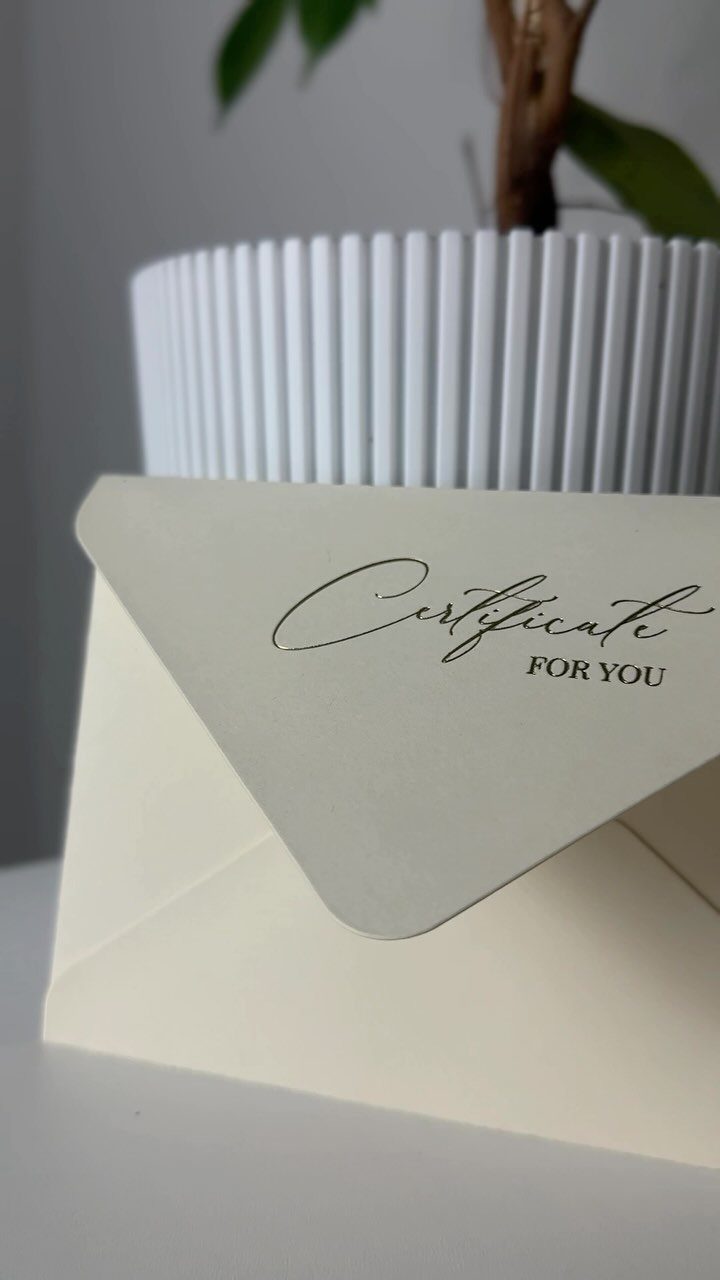 White gift certificate card in an envelope leaning against a white ribbed planter.