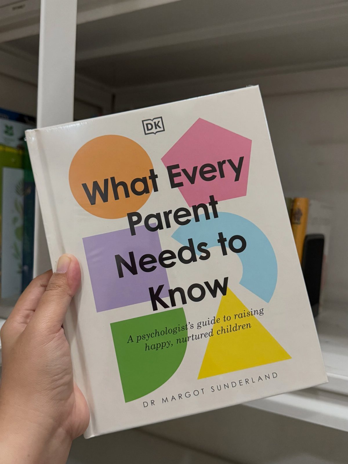 Hand holding a parenting book with colorful geometric shapes on the cover