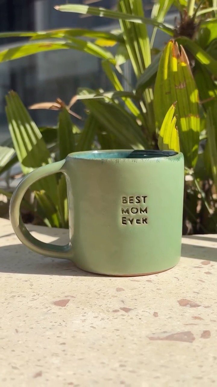 Light green ceramic mug with BEST MOM EVER text on a stone surface.
