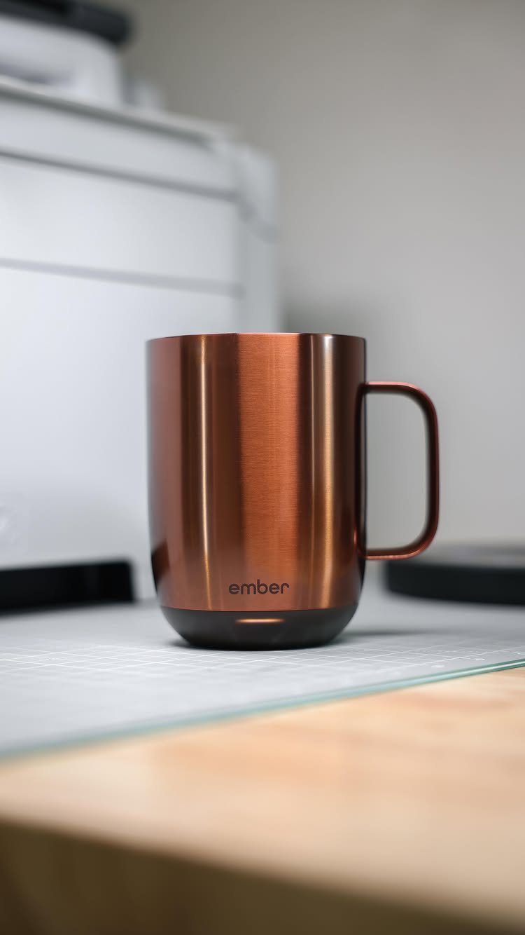 Copper Ember smart mug sitting on a desk with a blurred printer background.