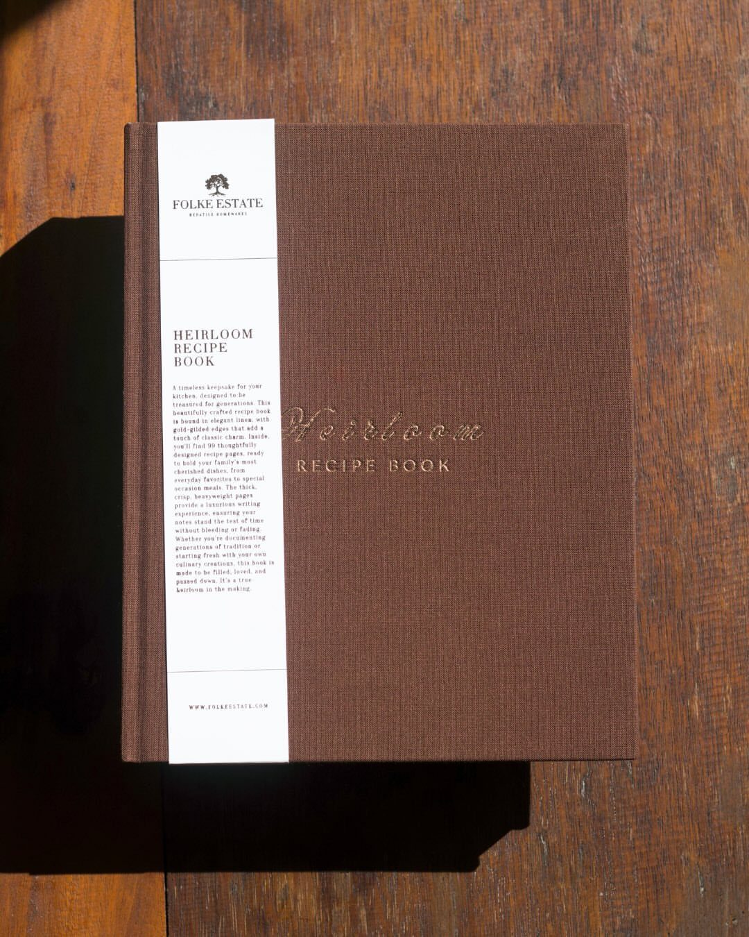 Brown linen heirloom recipe book with a white paper band on wooden table