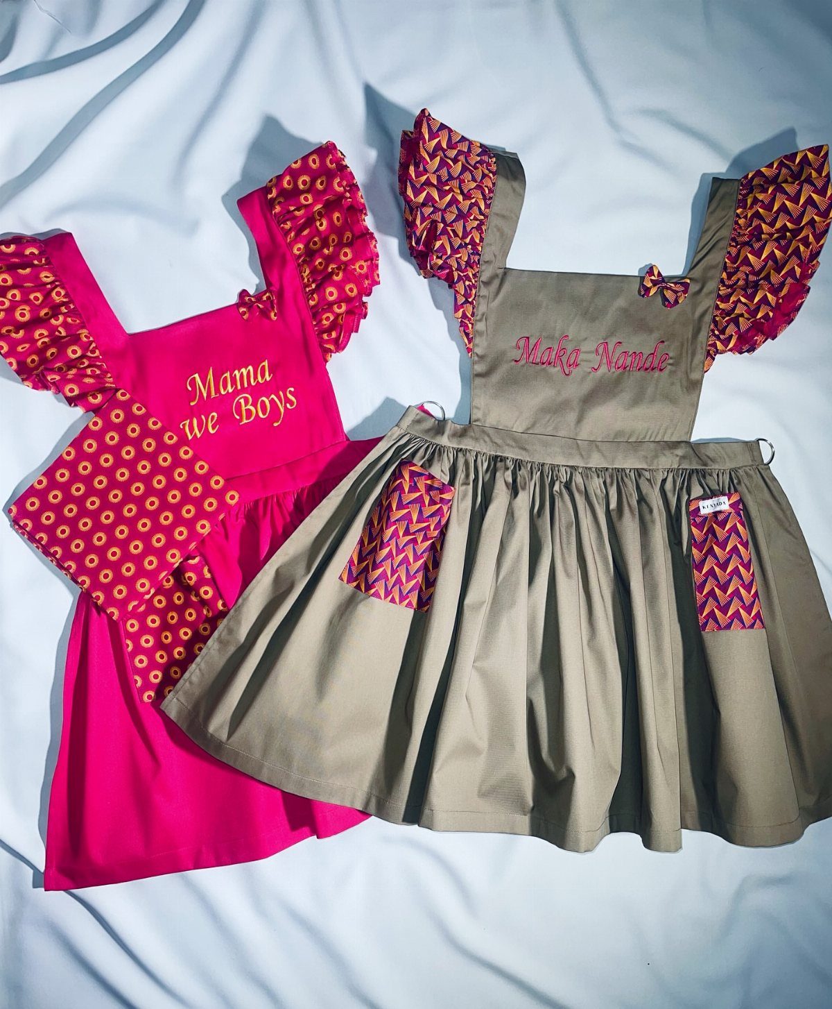 Two personalized aprons, one pink and one beige, with custom embroidery and ruffles.