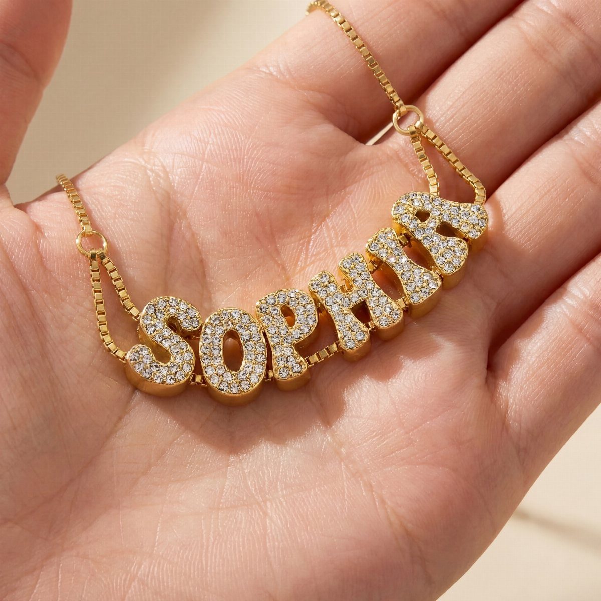 Gold nameplate necklace spelling SOPHIA with crystals held in a person's hand