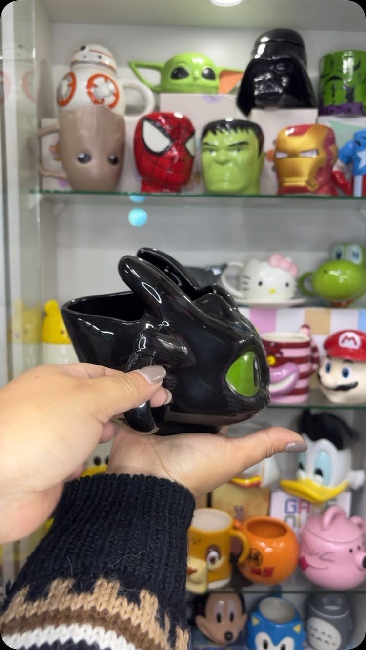 Black dragon-shaped ceramic mug held in hands with other character mugs behind.