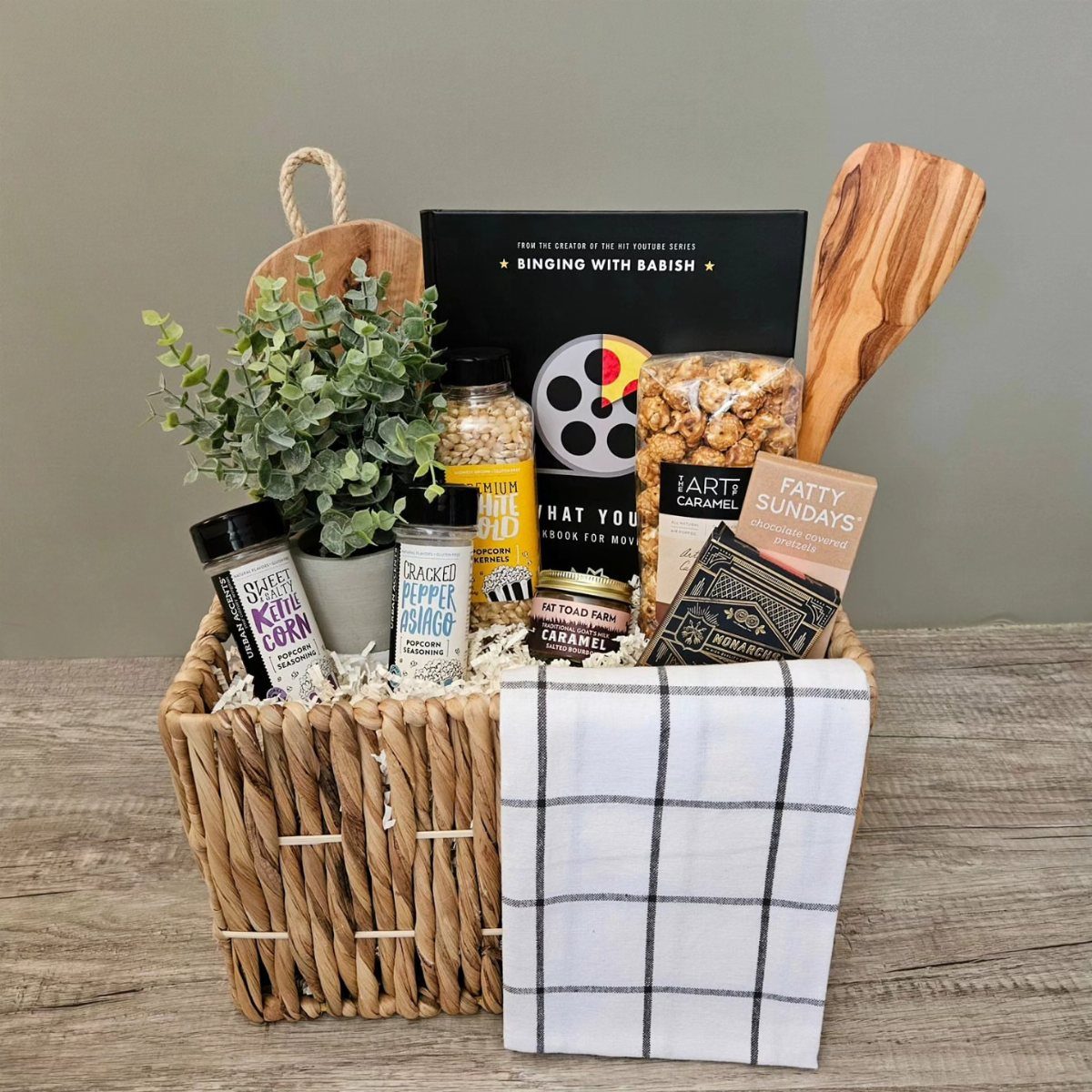 Woven gift basket filled with movie snacks, seasonings, and a cooking book.