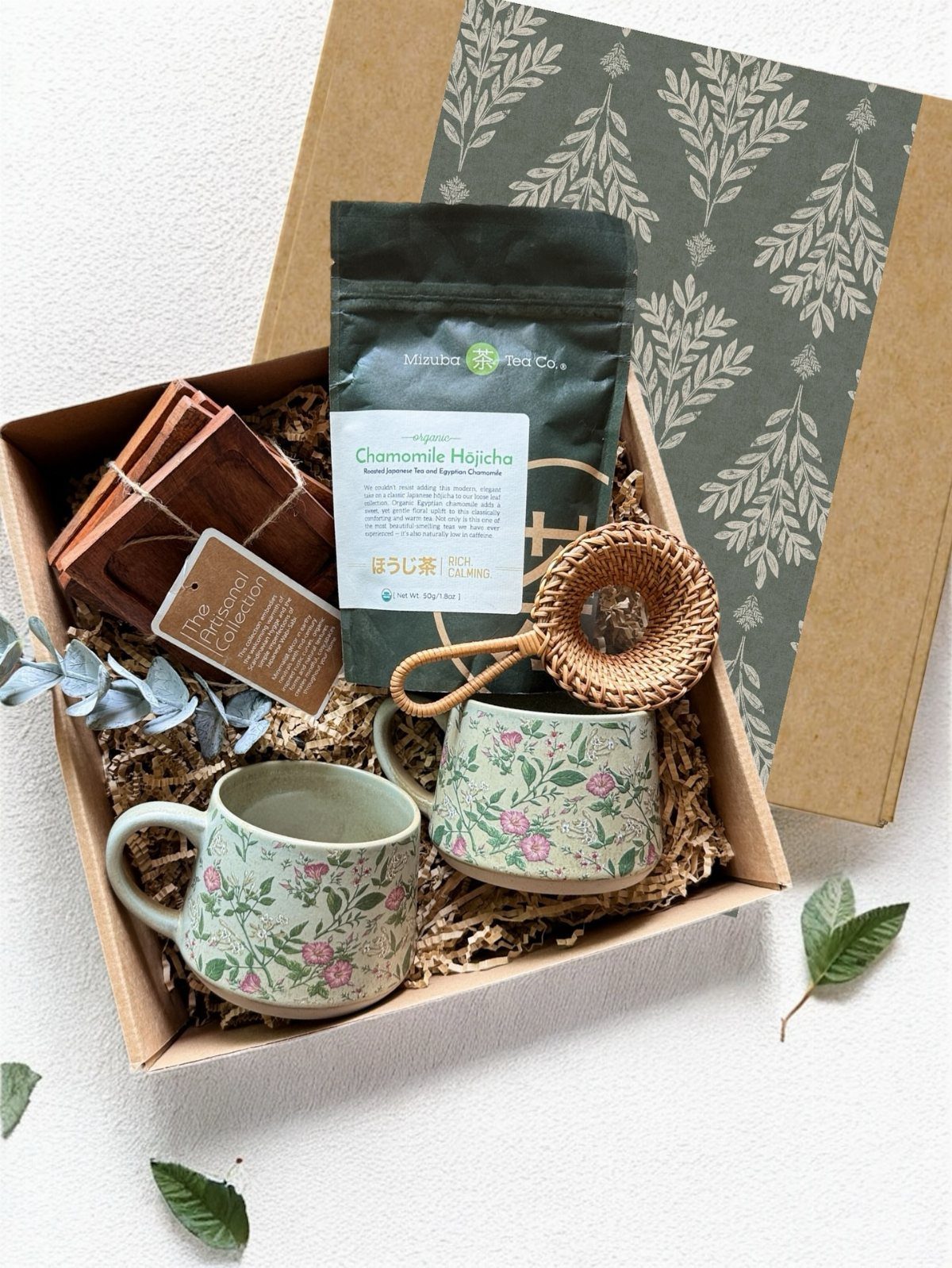 Two floral mugs and tea assortment in a gift box with shredded paper.