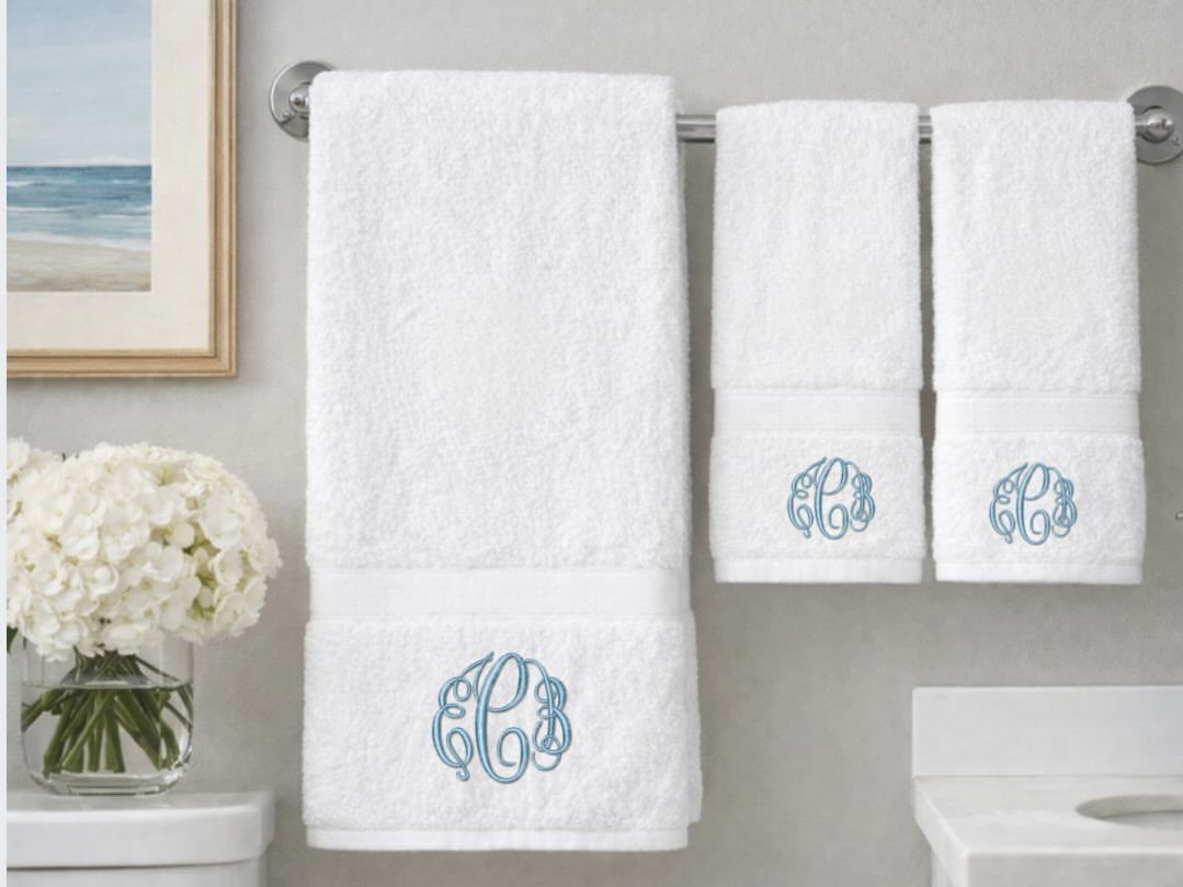 White towels with light blue embroidered monograms hanging on a silver bathroom rack.