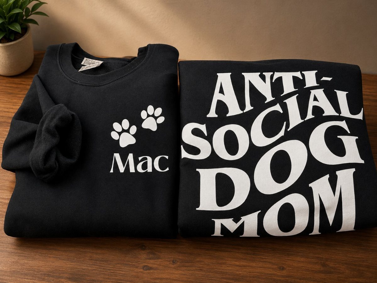 Two black sweatshirts with white text and paw prints on a wooden table