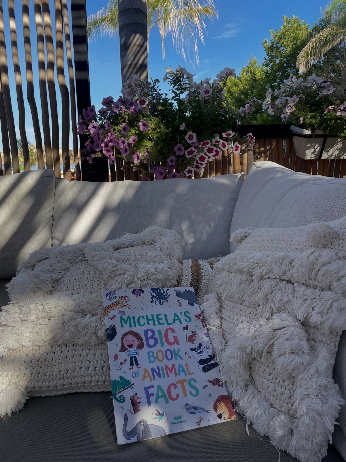 Children's book with a personalized name resting on a white outdoor sofa cushion.
