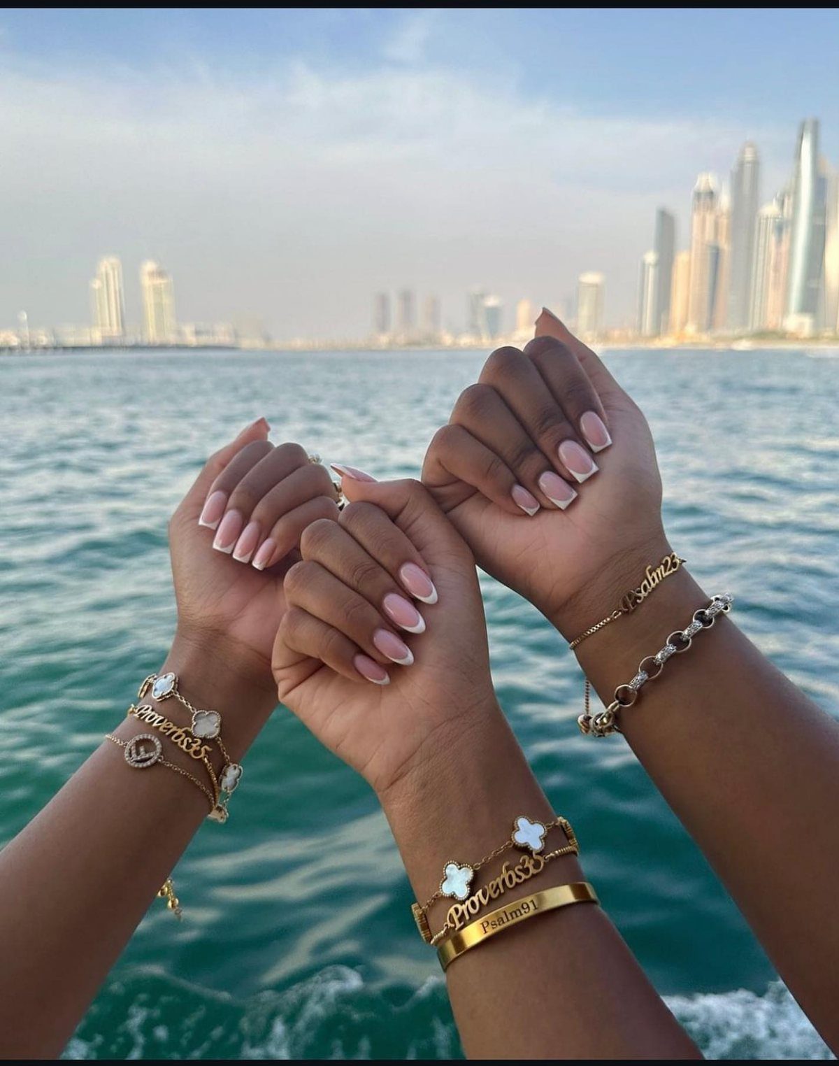 Three hands joined together wearing gold personalized engraved bracelets over a blue ocean.