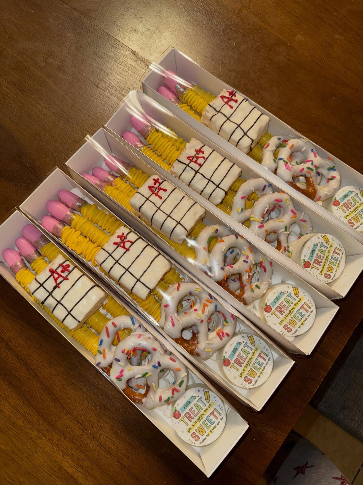 Four gift boxes containing chocolate-covered pretzels, A+ notebook treats, and yellow pencils.