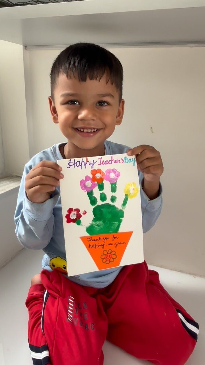 Young boy holding a handmade Teacher's Day card with a green handprint flower.