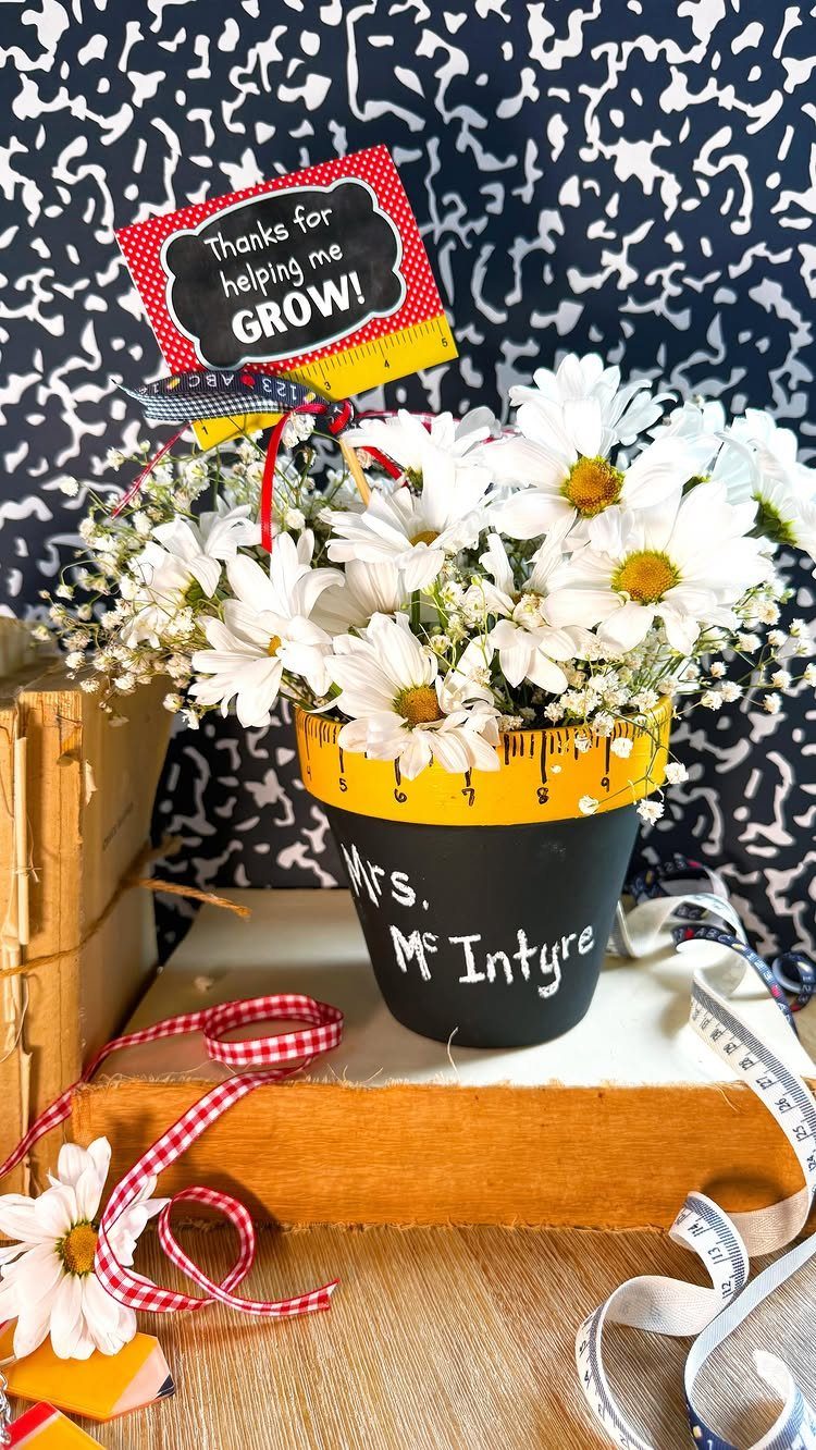 White daisies in a black pot with a thank you growth tag
