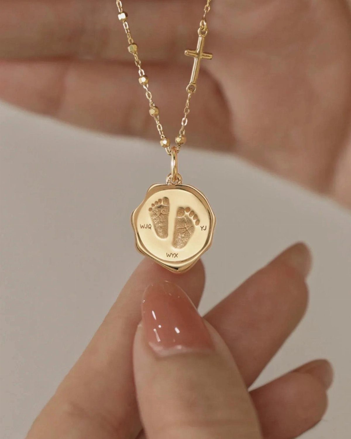 Gold necklace with a cross and a pendant engraved with baby footprints