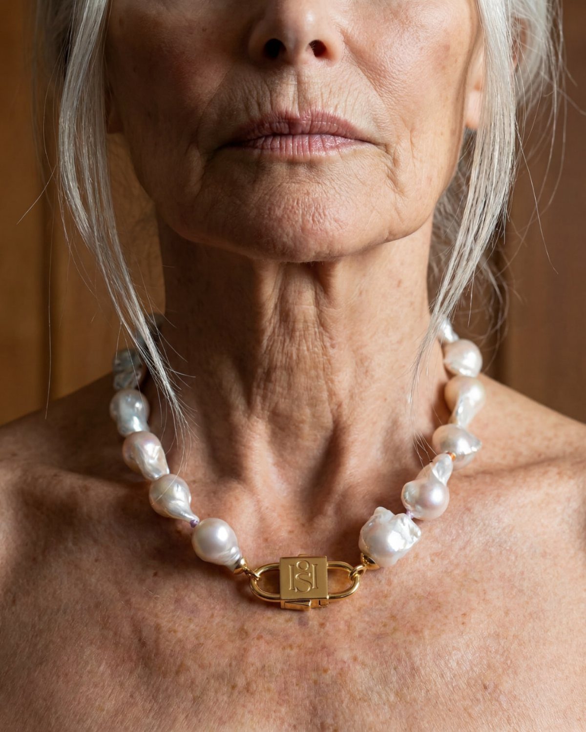 Older woman wearing a necklace of large white baroque pearls with a gold clasp.