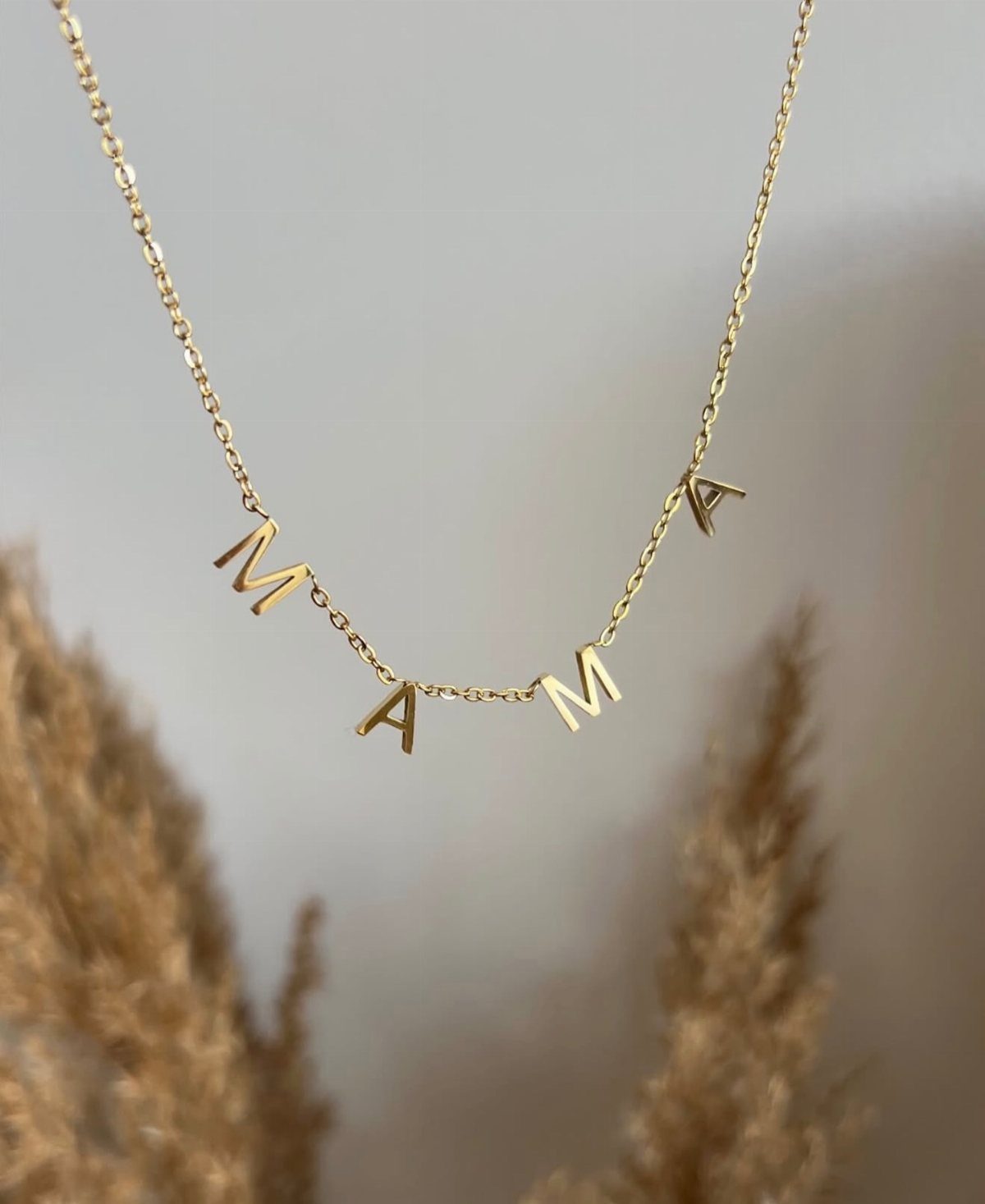 Gold chain necklace with letters spelling MAMA against a neutral, soft background