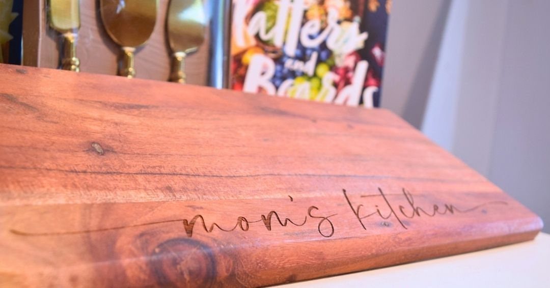 Wooden cutting board engraved with the words mom's kitchen in cursive script
