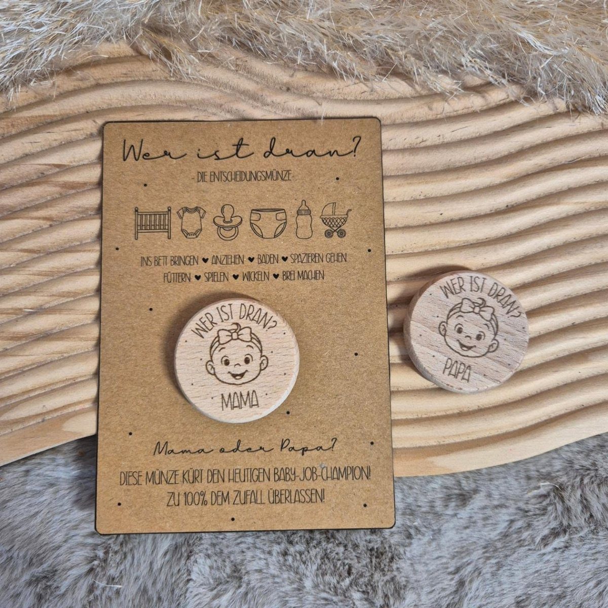 Two wooden decision coins for parents with baby illustrations on a cardboard card.