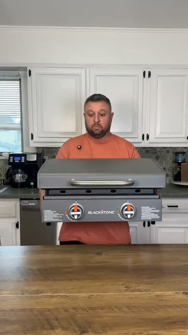 Man holding a grey Blackstone tabletop griddle in a bright white kitchen.