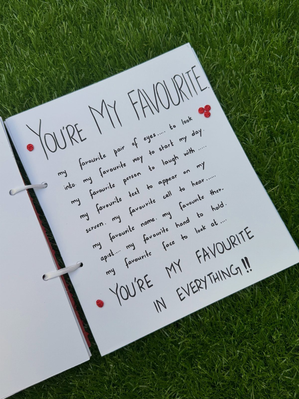 Handwritten romantic fill-in-the-blank book pages resting on a lush green grass background.