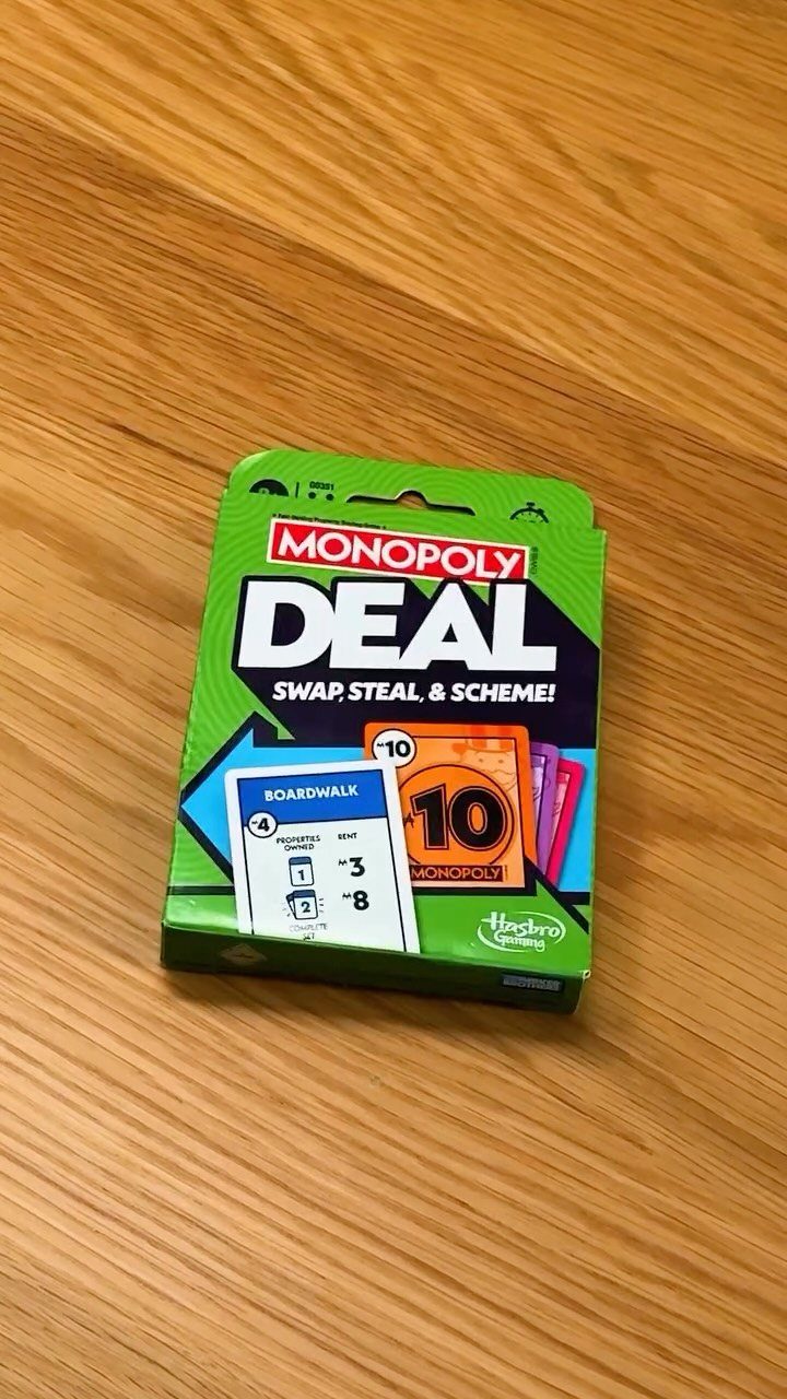 Monopoly Deal card game box on a light brown wooden table surface.