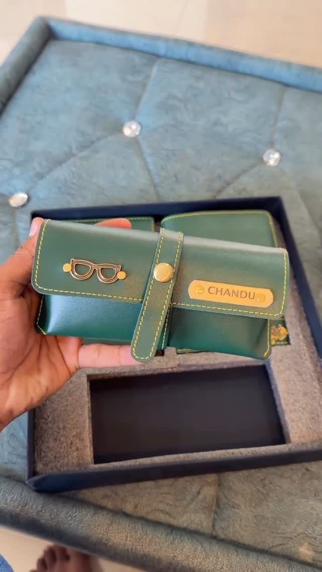 Green leather wallet with gold nameplate and glasses charm held over gift box
