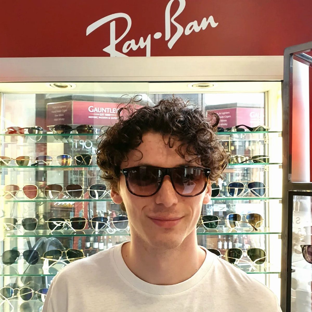 Young man wearing black Ray-Ban sunglasses standing in front of a sunglasses display.