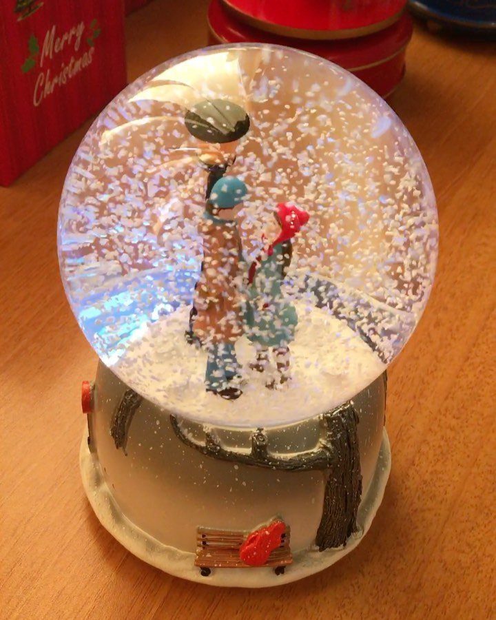 Snow globe with a couple figurine inside surrounded by falling white snow glitter.