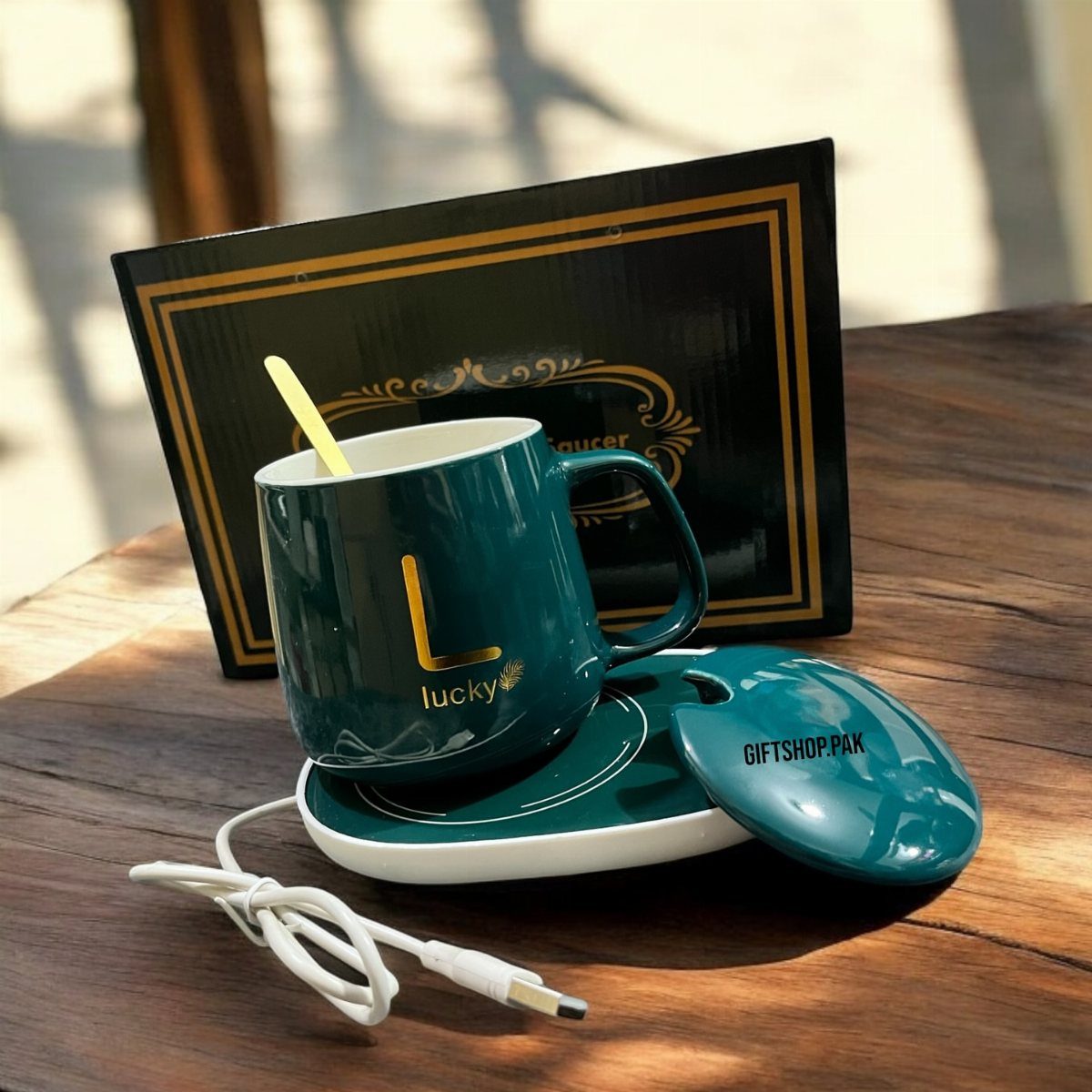 Dark green ceramic mug on a white electric warming coaster with a gift box.