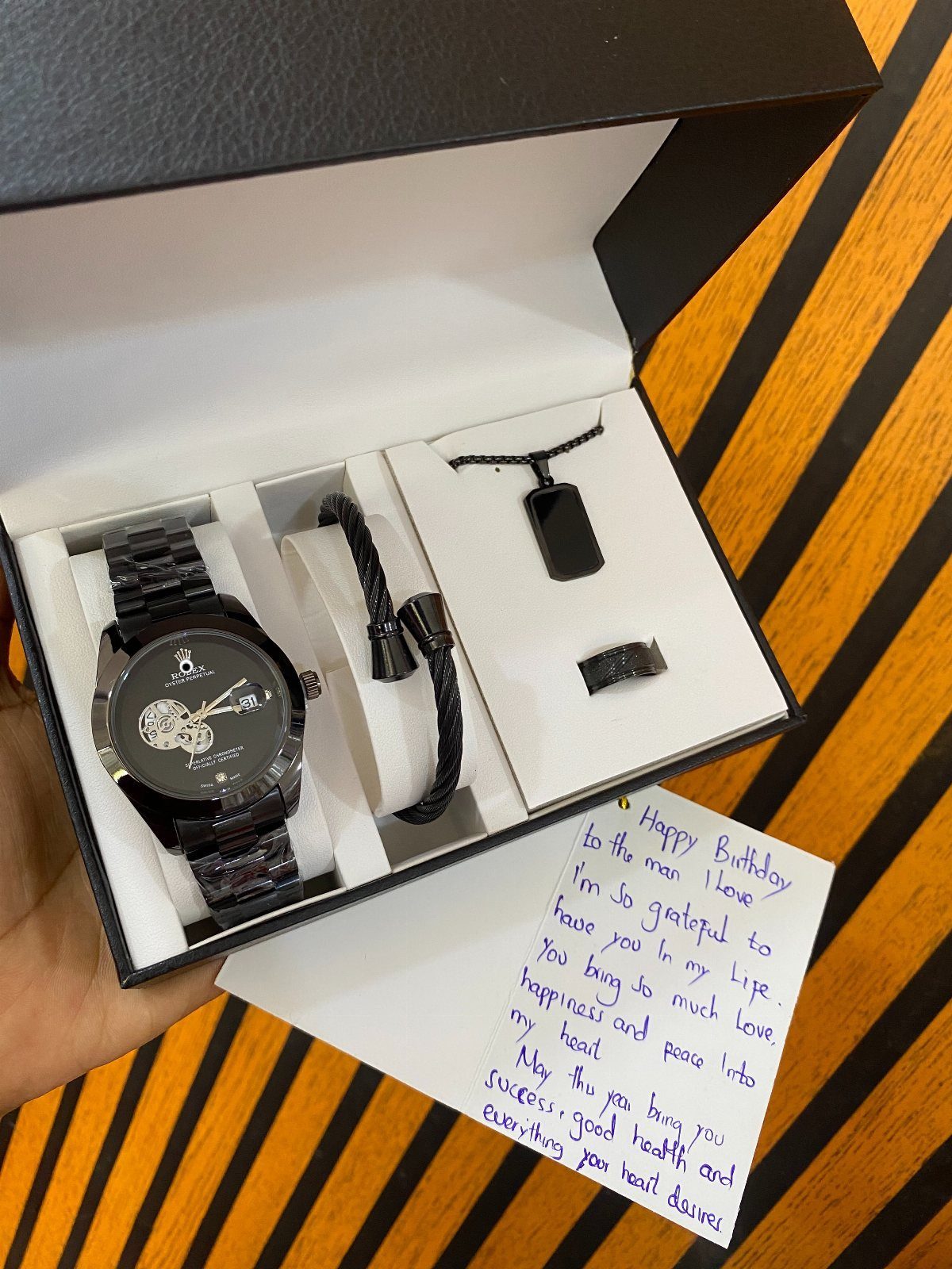 Black wristwatch, bracelet, and necklace in a gift box with a handwritten note.