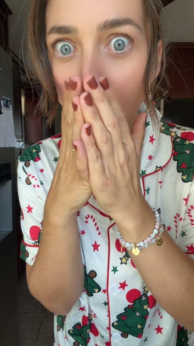 Woman in white Christmas pajamas with tree patterns looking surprised with hands over mouth