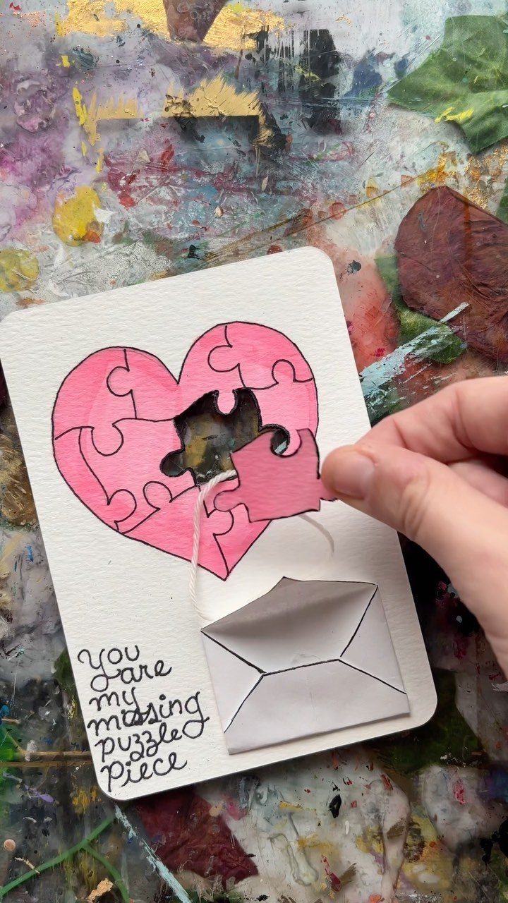 Hand placing a pink puzzle piece into a heart-shaped puzzle on a card.