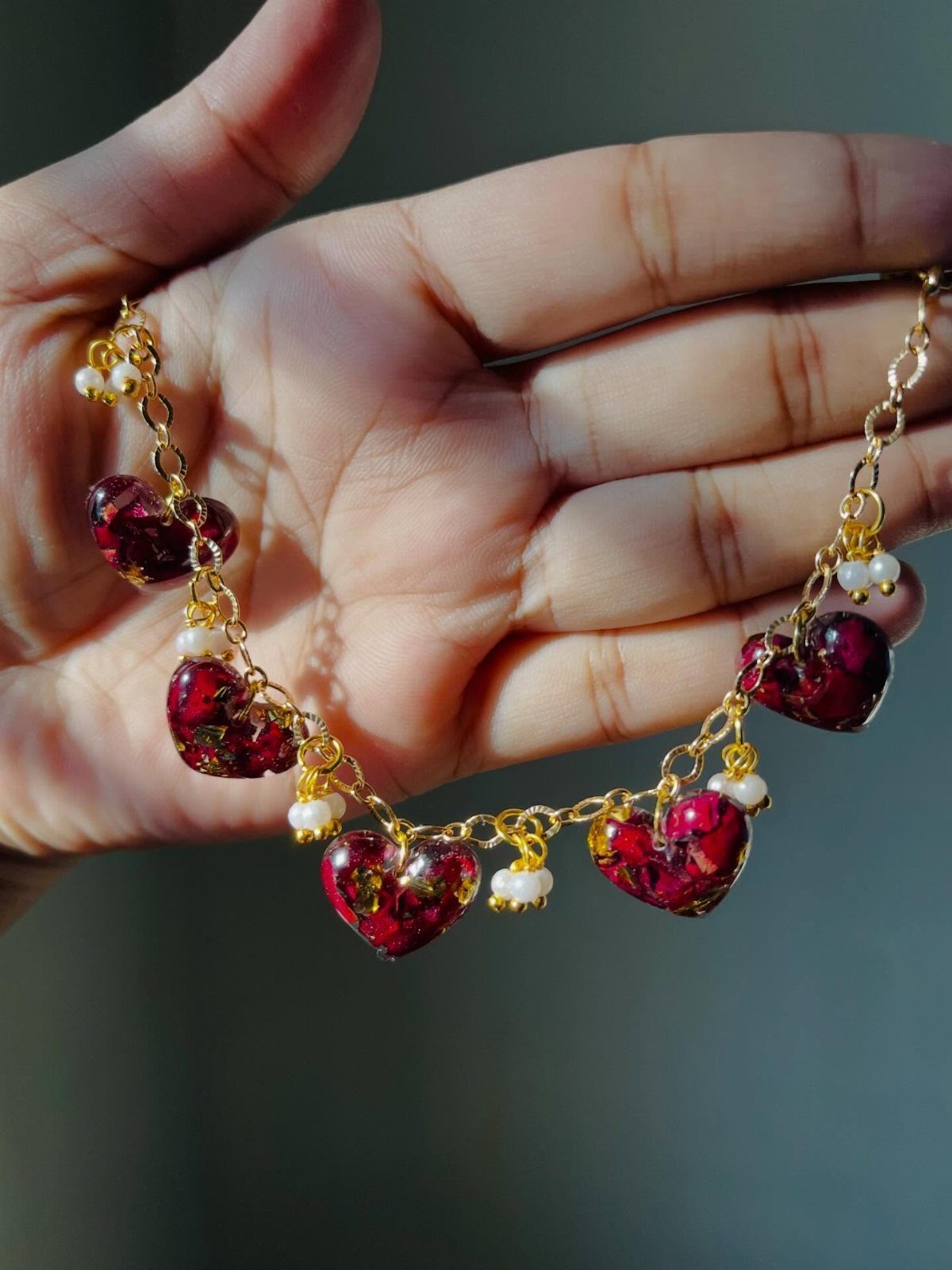 Gold chain bracelet with red heart resin charms and pearls in a hand