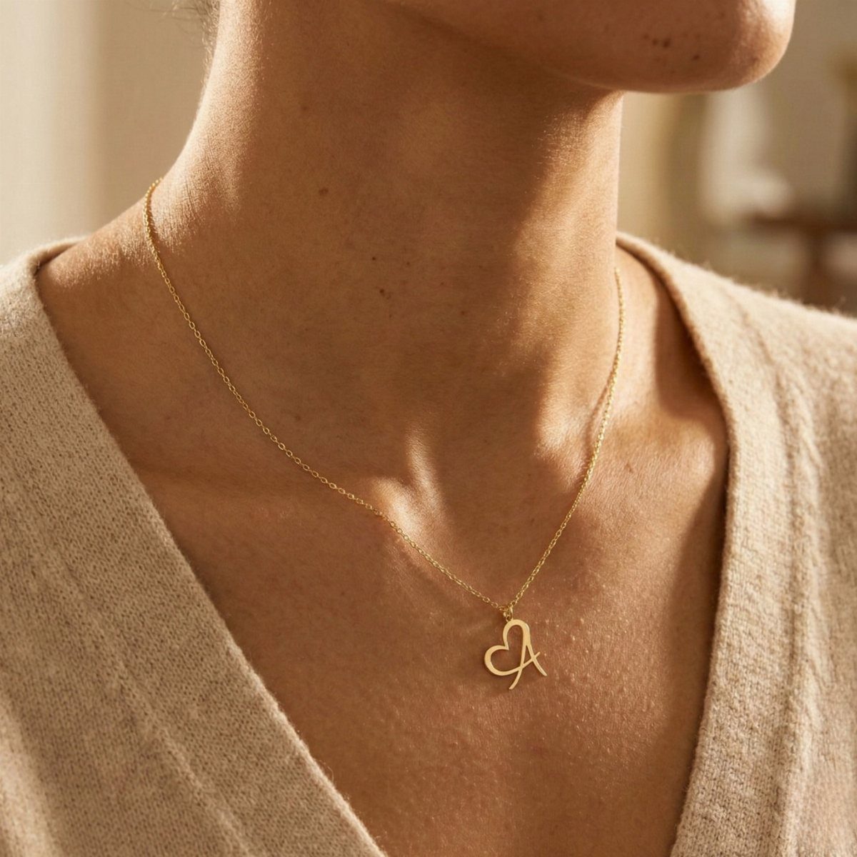 Gold heart necklace with letter A worn over a beige sweater