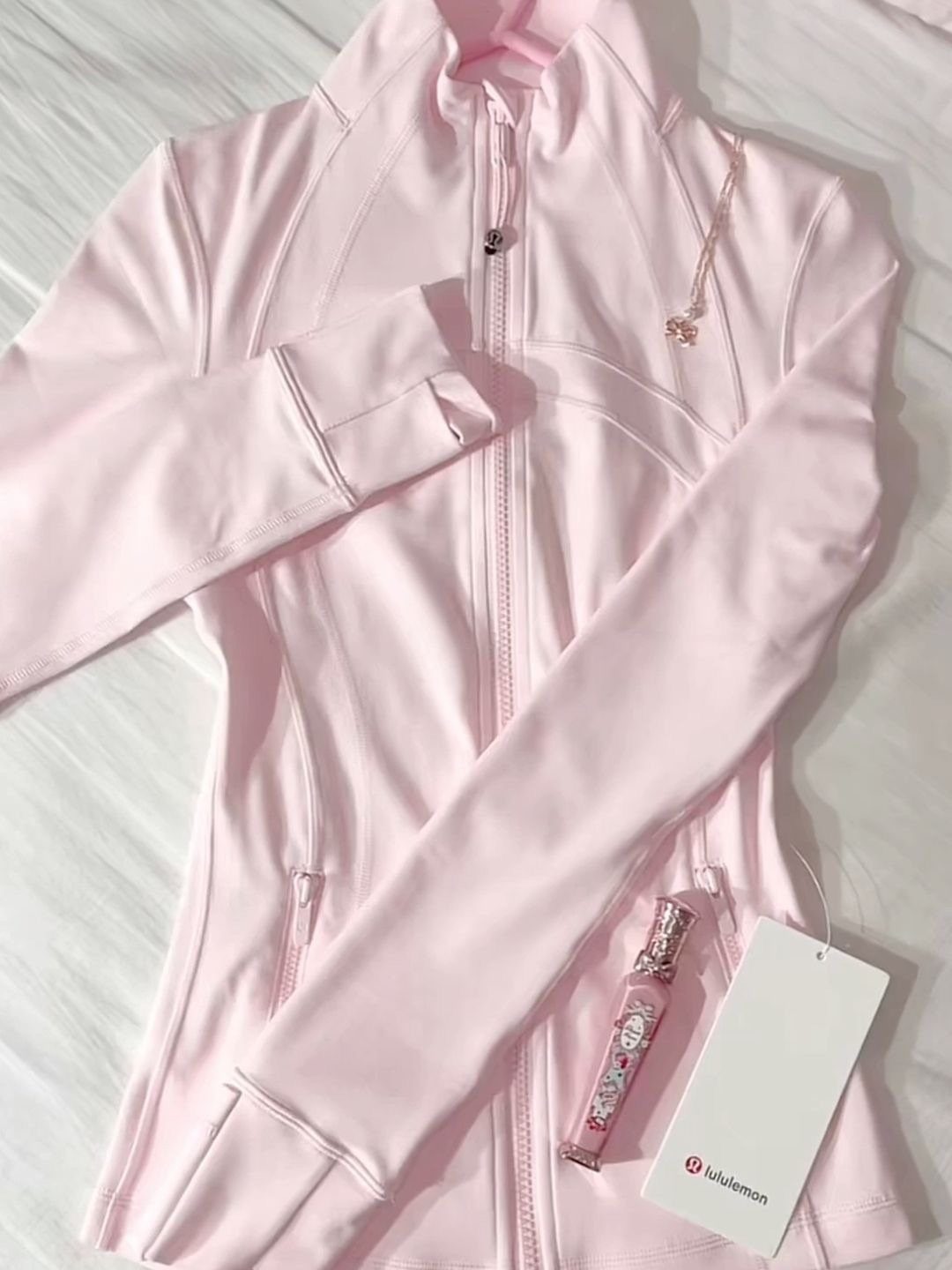 Light pink Lululemon zip-up jacket with a gold necklace and perfume bottle.