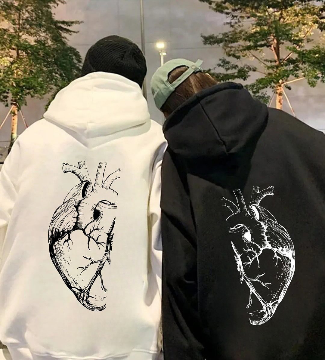 Two people wearing matching white and black hoodies with anatomical heart prints.