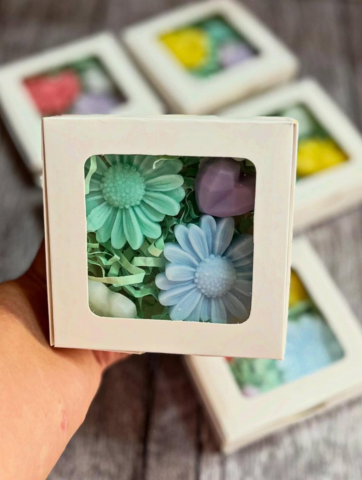 Small white gift box containing colorful flower and heart shaped soaps.
