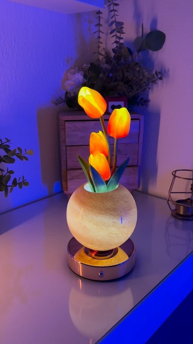Glowing orange tulip lamp in a round vase on a reflective white table