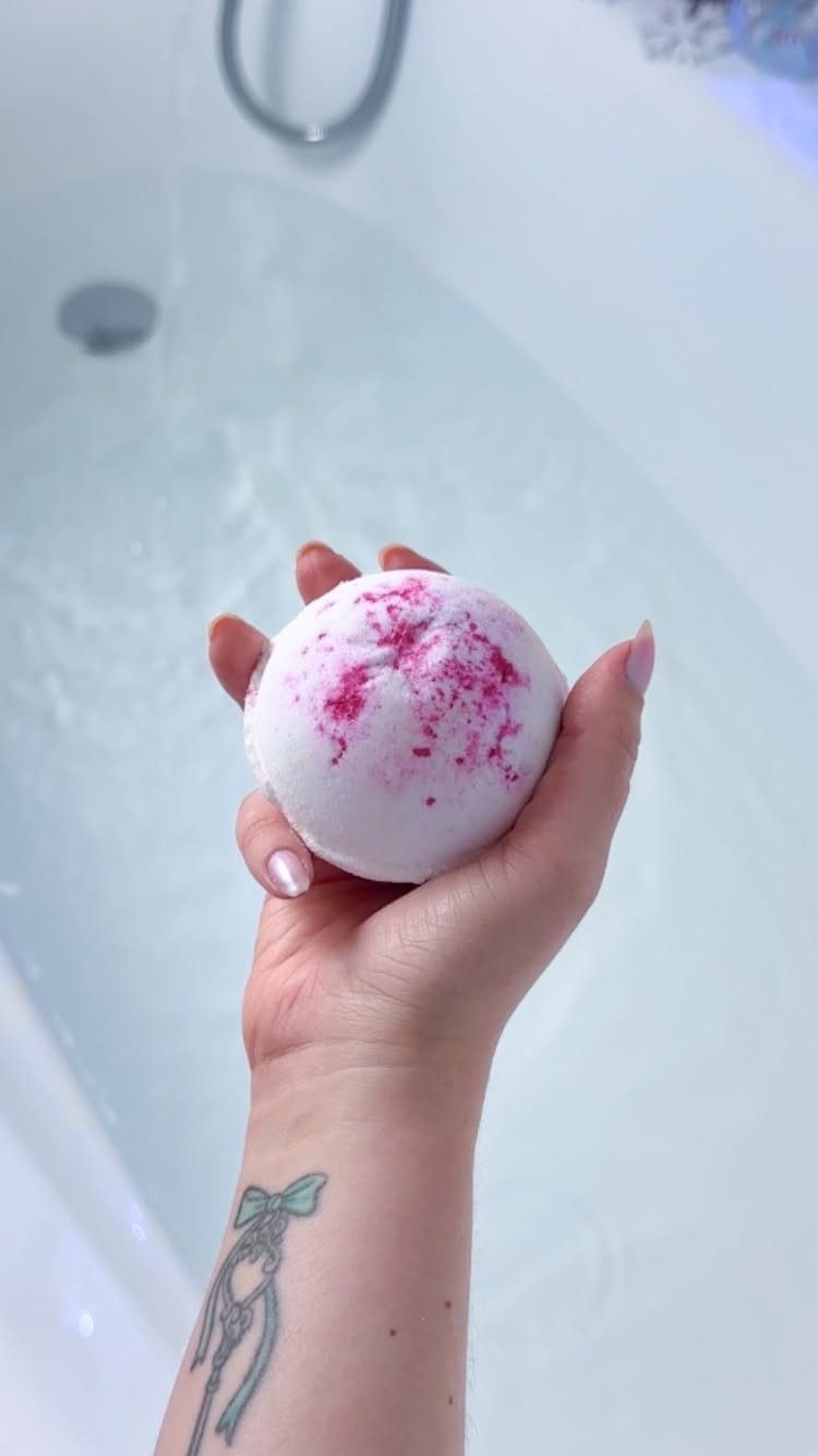 Hand holding a white and pink bath bomb over a white bathtub