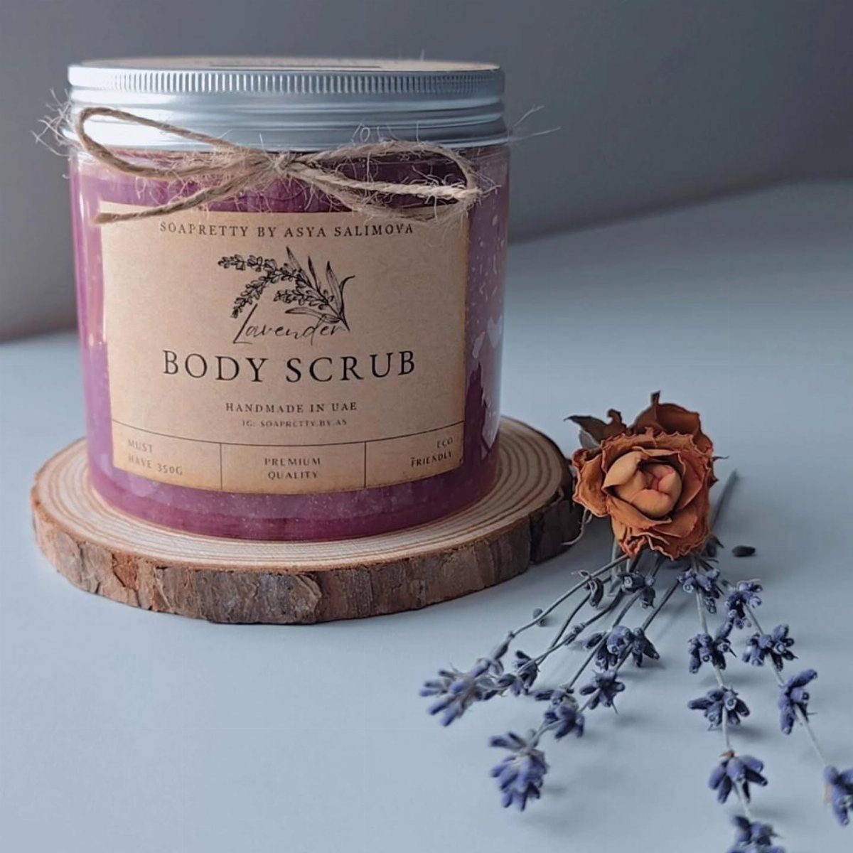 Lavender body scrub in a glass jar on a wooden slice with dried flowers